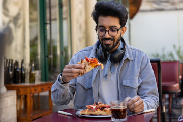 Young hindu man eating pizza in pizzeria