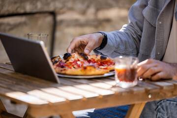 Man sitting at the table, eating pizza and working on laptop