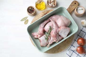 Raw rabbit meat in baking dish and products on white wooden table, flat lay. Space for text