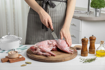 Woman cutting whole raw rabbit at white wooden table, closeup