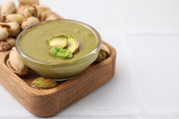 Tasty pistachio cream in bowl and nuts on white tiled table, closeup. Space for text