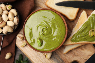 Tasty pistachio cream, toasts and nuts on wooden table, top view