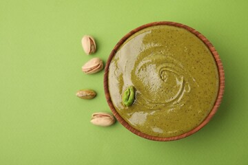 Tasty pistachio cream in bowl and nuts on green background, top view. Space for text