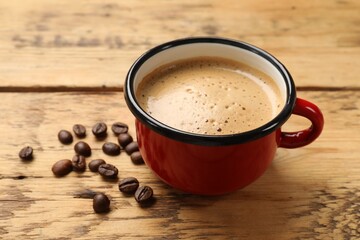 Cup of aromatic coffee and beans on wooden table, closeup