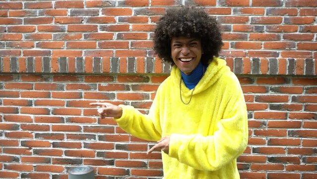 Smiling young Afro-Mexican man pointing to empty space against a red brick wall