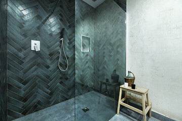 A large shower cubicle with green tiled tempered glass screen and gray floor