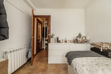 A youth bedroom with a single bed, aluminum radiator and a white dresser with many drawers