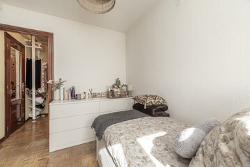 A youth bedroom with a single bed, aluminum radiator, clothes hanging on a shelf outside the room