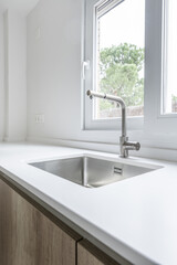 Kitchen faucet with stainless steel bowl embedded in the countertop under an aluminum window
