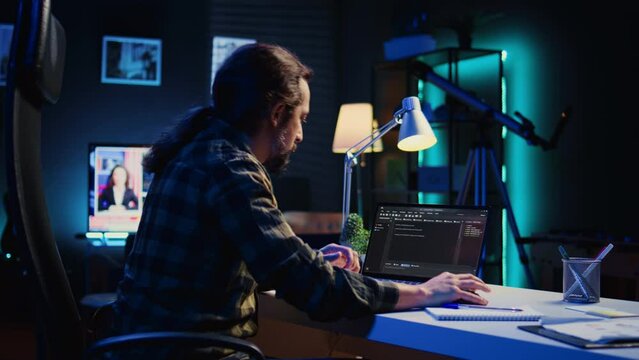 Experienced programmer writes code on laptop screen while in apartment office using Java programming languages. Developer remotely working on fixing database errors while working from home, camera B