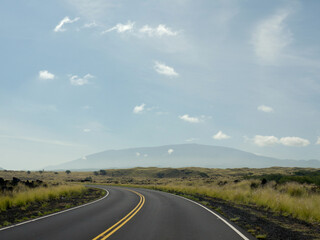 Driving to distant Mauna Kea volcano by Saddle road with green fields on road sides on beautiful sunny day on Big Island of Hawaii