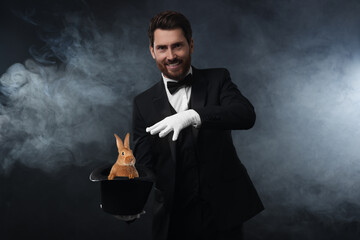 Magician showing trick with top hat and rabbit in smoke on dark background
