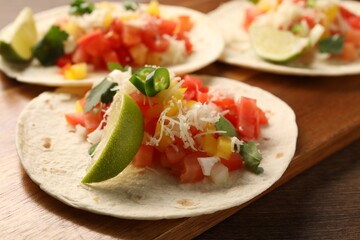 Delicious tacos with vegetables and lime on wooden table, closeup