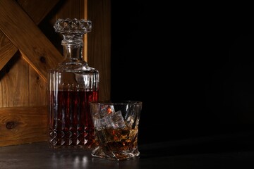 Whiskey in glass and bottle near wooden crate on dark table against black background. Space for text