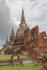 Fototapeta premium Traditional Thai stone pagoda building structure and red brick ruins at Wat Phra Si Sanphet temple in Ayutthaya Thailand historical park on a cloudy day