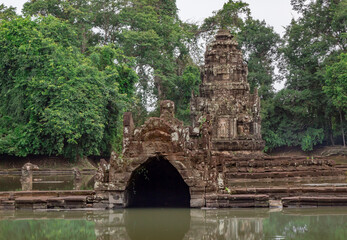 Fototapeta na wymiar Stone beautiful a temple ruin building architecture and Neak Pean dragon pagoda on water lake in Angkor Wat complex historical site in the jungle forest of Seim Reap Cambodia on a cloudy overcast day