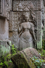 Woman design stone carving and moss covered green bricks ruin building exterior at the Banteay Kdei Temple complex wall. Angkor Wat historical site, Siem Reap, Cambodia