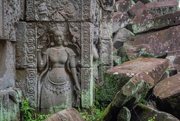 Woman stone carving and moss covered green stone ruin building exterior and bricks at the Banteay...