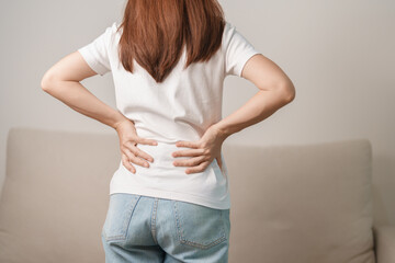 woman having back body ache during sitting on Couch at home. adult female with muscle pain due to...