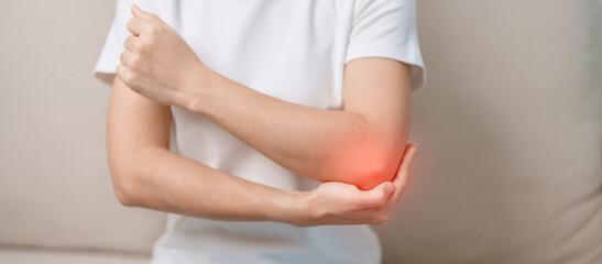 Woman having elbow ache during sitting on couch at home, muscle pain due to lateral epicondylitis...