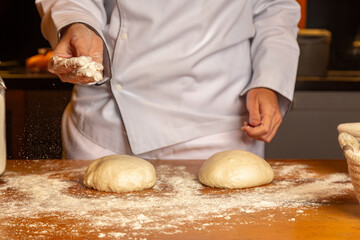 mão de chef jogando farinha e preparamdo a massa de pão artesanal  na cozinha - obrazy, fototapety, plakaty
