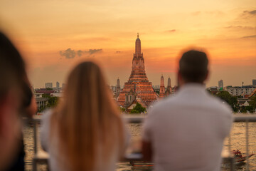 Fototapeta na wymiar Wat Arun Temple in sunset, Tourists enjoy the view to Temple of Dawn near Chao Phraya river. Take photo from rooftop bar. Landmark and Travel destination in Bangkok, Thailand and Southeast Asia