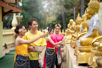 Songkran Festival - Young Asians Wearing Thai Clothes Pose Happily Playing in the Water During Songkran Festival, Buddha Statue Bathing Ceremony During Songkran Festival, Splashing water. - obrazy, fototapety, plakaty