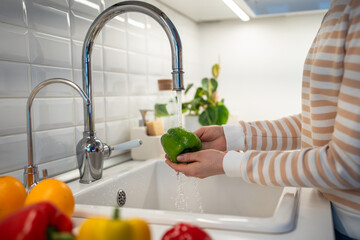 Hands washing green paprika pepper at home. Preparation of fresh salad. Vegetables on worktop near...