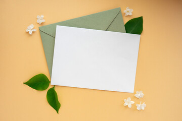Composition with empty envelope and beautiful spring lilac flowers on beige background. Mockup card invitation greeting card postcard copy space template. Branches of lilac blooming bouquet.