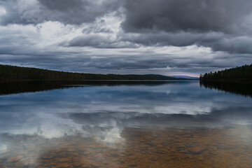 Burusjön mountain lake in Idre Dalarna Sweden forest at dusk with cloudscape. Clear water with pebbles, reflection of dramatic clouds and trees in the water