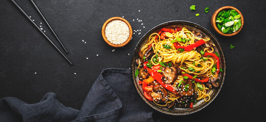 Vegan stir fry noodles with red paprika, champignons, green onion and sesame seeds with ginger, garlic and soy sauce.. Black table background, top view