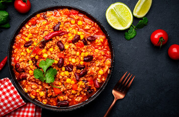 Chili con carne, mexican dish with minced beef, red beans, paprika, corn, cilantro and red peppers in spicy tomato sauce, tex-mex cuisine, black table background, top view