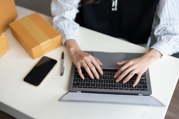Closeup of hand typing work of Asian female online shopping business owner There was a laptop keyboard, smartphone, pen and parcel box nearby. List of products prepared for export to the world market