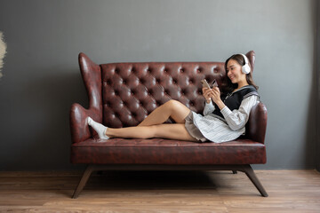 Obraz premium Young Asian woman resting and shopping online with a credit card and using a smartphone Sitting listening to music with my ears through a listening application on the sofa in my house.