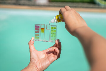 Action of person hand is using water tester kit with chemical to measuring Chlorine concentration of the swimming pool (as blurred background). - obrazy, fototapety, plakaty