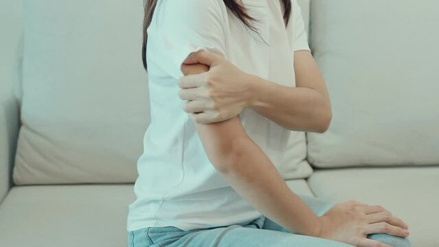 Woman having arm pain during sitting on couch at home, muscle injury and ache. Health and medical concept