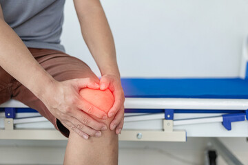 Close-up of a man holding his knee in discomfort. Suffering from knee pain while sitting on bed at...