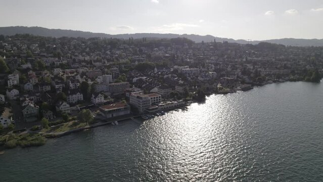Drone shot flying near the city of Thalwil at the Zurich Lake in Switzerland  on a sunny day with water and boats around the shore and white houses in the city LOG
