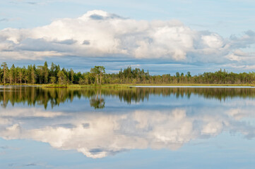 Fototapeta premium A tranquil partly cloudy summer evening by a lake with perfect reflection on the water surface, Northern Europe