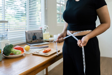 overweight Asian woman measuring her hip while learning to make salad and healthy food from social...