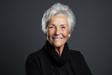 Portrait of a happy senior woman in black over grey background.