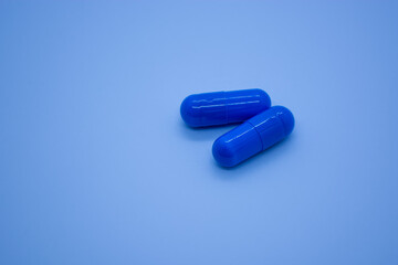 Two blue pills on blue background. Focus on foreground, shallow DOF. Close-up. Theme is treatment of diseases, medicine and pharmaceuticals.