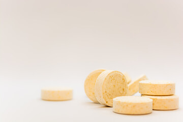 Tablets with a yellow tint with small inclusions of visible raw materials on a white creamy pastel background. Close-up. Selective focus. Theme is treatment of diseases, medicine and pharmaceuticals.