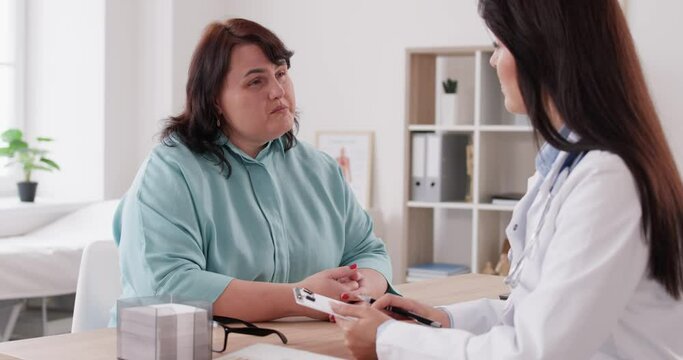 Fat, overweight patient consults with a doctor, specializing in nutrition, during a clinic visit at the hospital. The medical professional addresses weight related concerns, fostering a healthcare.