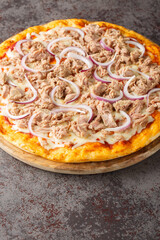 Pizza Tuna is an unusual and tasty combination of tomato sauce, canned tuna, mozzarella cheese and red onion close-up on a wooden board on the table. Vertical
