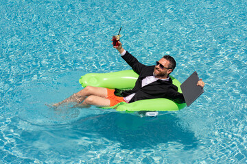 Business man in suit drink summer cocktail and using laptop in swimming pool. Travel business tourism. Office employee using laptop in pool on summer day. Successful businessman dreams in summer pool.