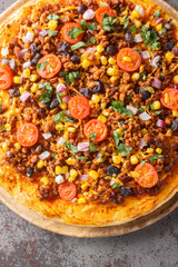 Tex Mex food Mexican American pizza with ground beef, vegetables, cheddar cheese close up on a wooden board on the table. Vertical top view from above