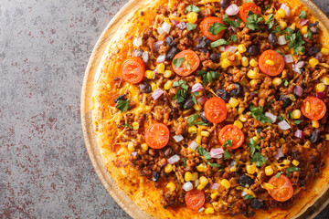 Hot Tex Mex taco pizza with ground beef, salsa, cheddar cheese and Mexican spices close-up on a wooden board on the table. Horizontal top view from above