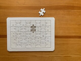 the last piece of an all-white jigsaw puzzle put on the light brown rubber wooden table with the copy space on the right side of the frame, valentine concept