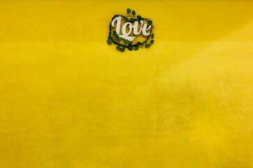 the white word “love” with green leaf is attached to the yellow wall with copy space at the bottom of the frame, valentine concept